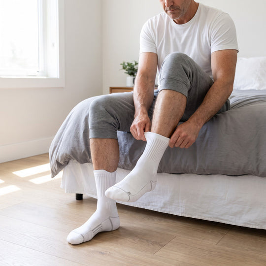 Man putting on white V-Socks compression socks in his bedroom