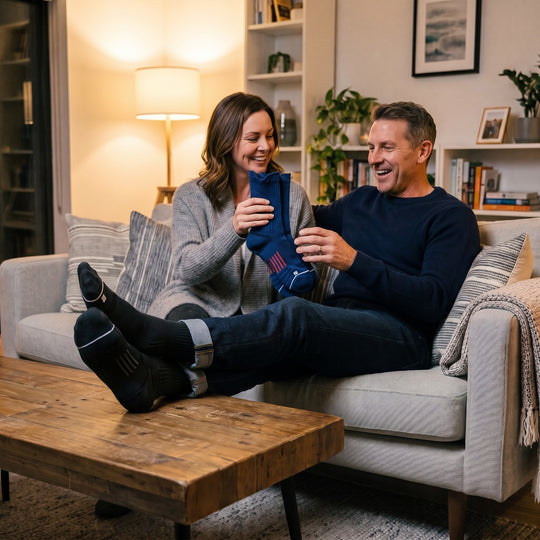 Wife offering her husband a pair of navy V-Socks compression socks on the sofa